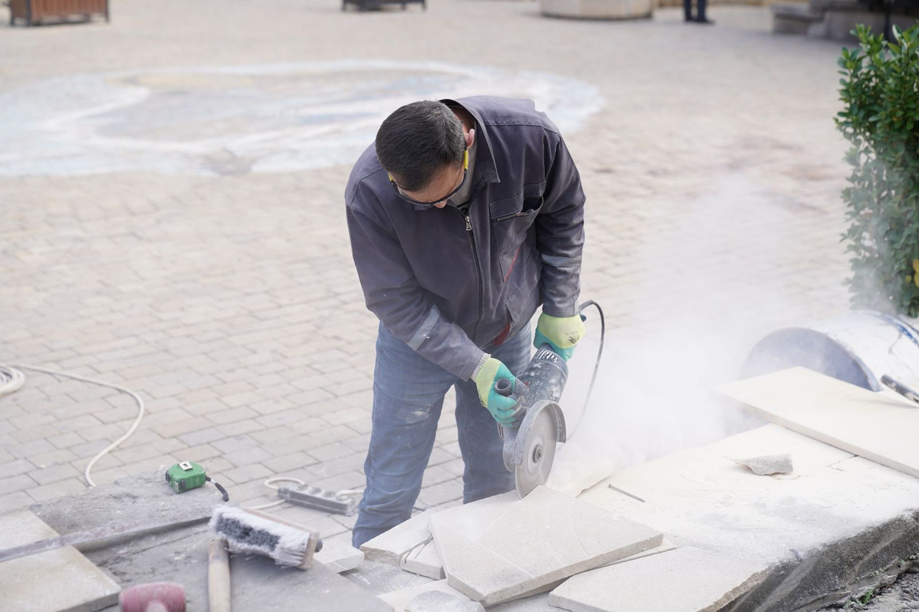 A mason cutting a pale stone slab with a diamond-blade grinder